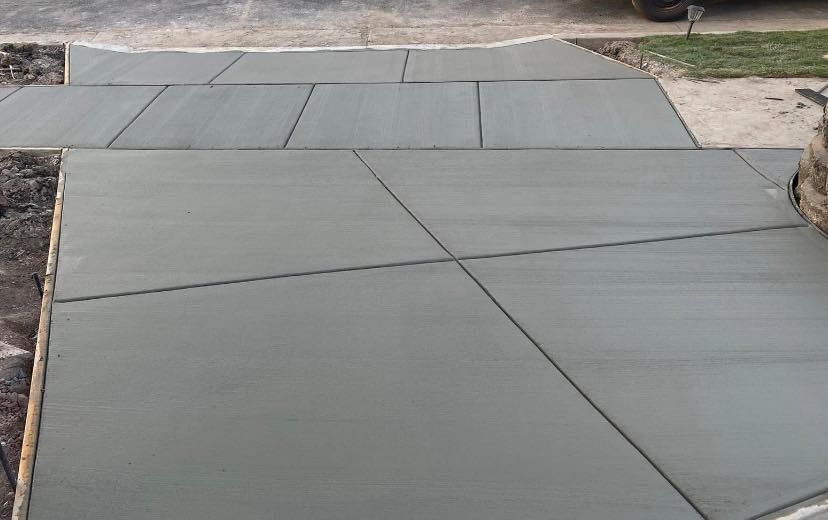 A newly poured concrete driveway featuring a geometric grid of saw-cut control joints in a residential setting.