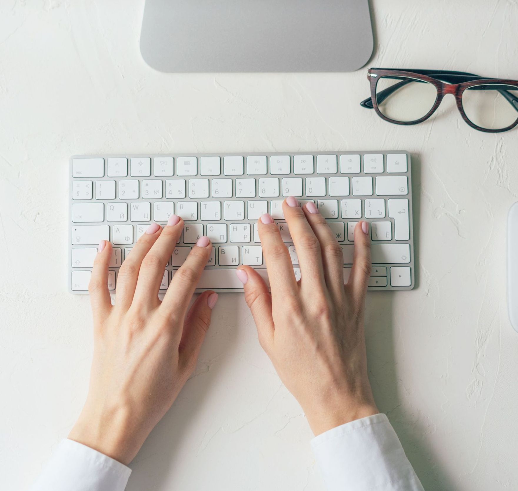 A person 's hands are typing on a white keyboard.