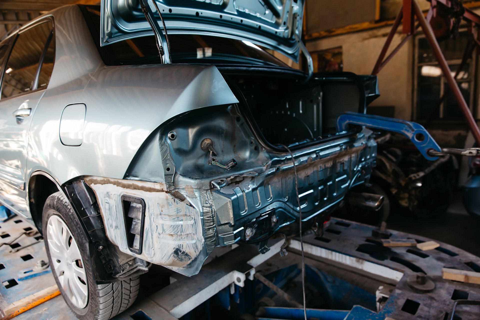 A car is being repaired in a garage with the hood up.
