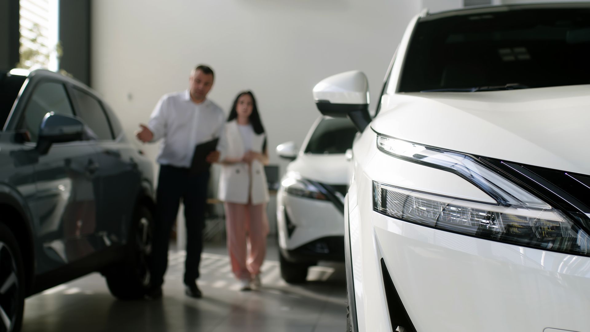 A man and a woman are looking at a car in a showroom.