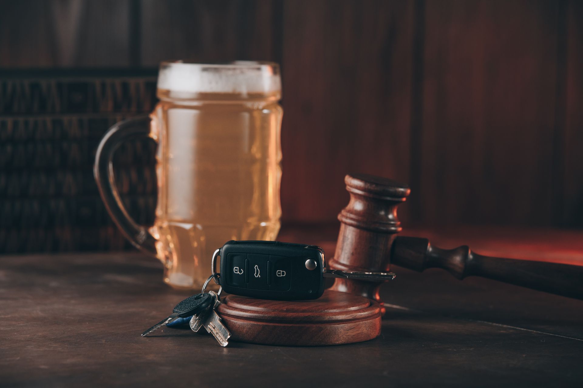 Beer mug, car keys, and gavel on a wooden surface, suggesting a DUI or legal context.