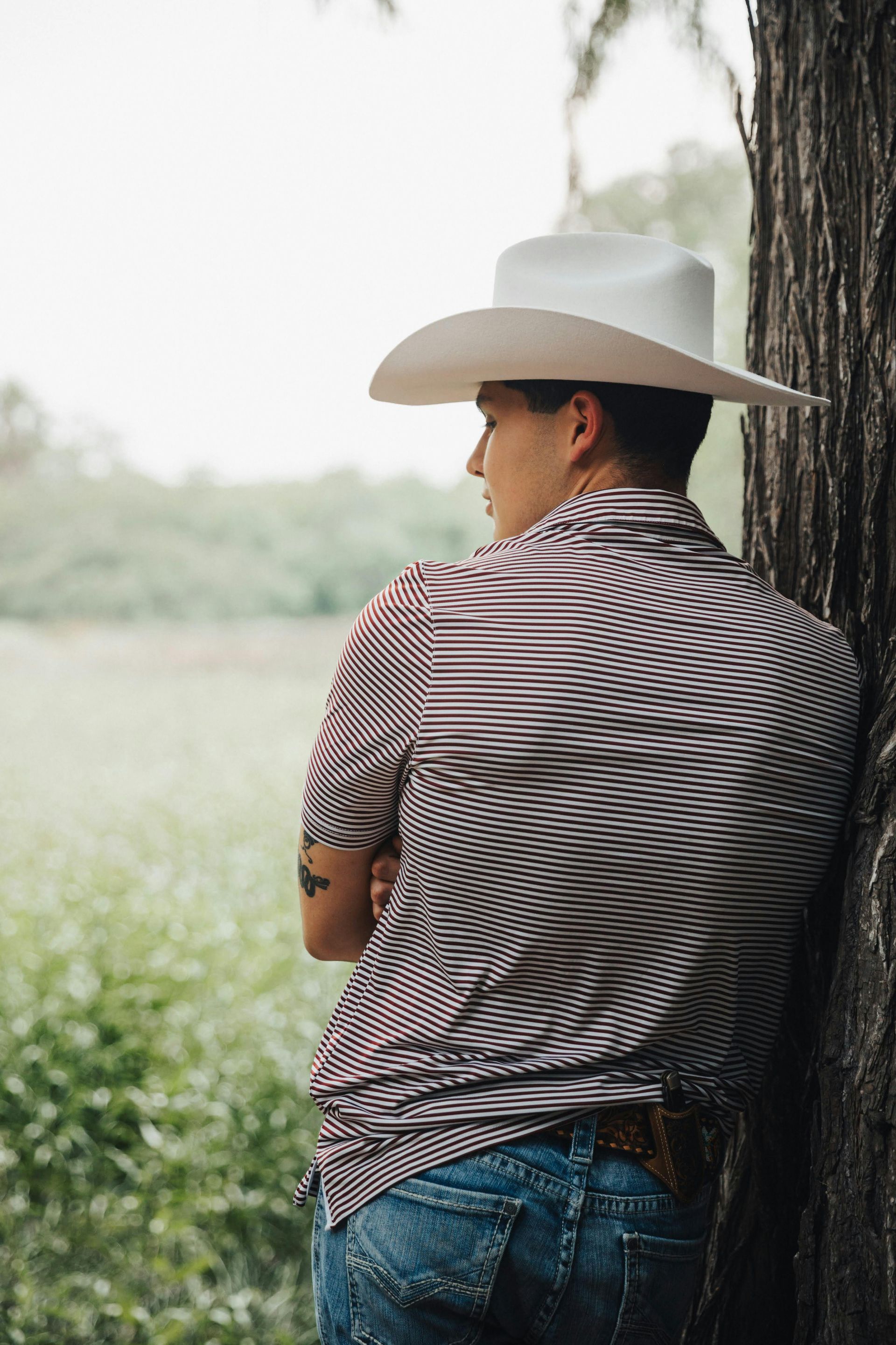 A man wearing a cowboy hat is leaning against a tree.