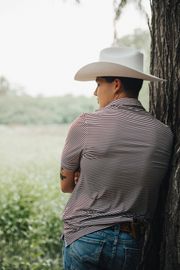 A man wearing a cowboy hat is leaning against a tree.