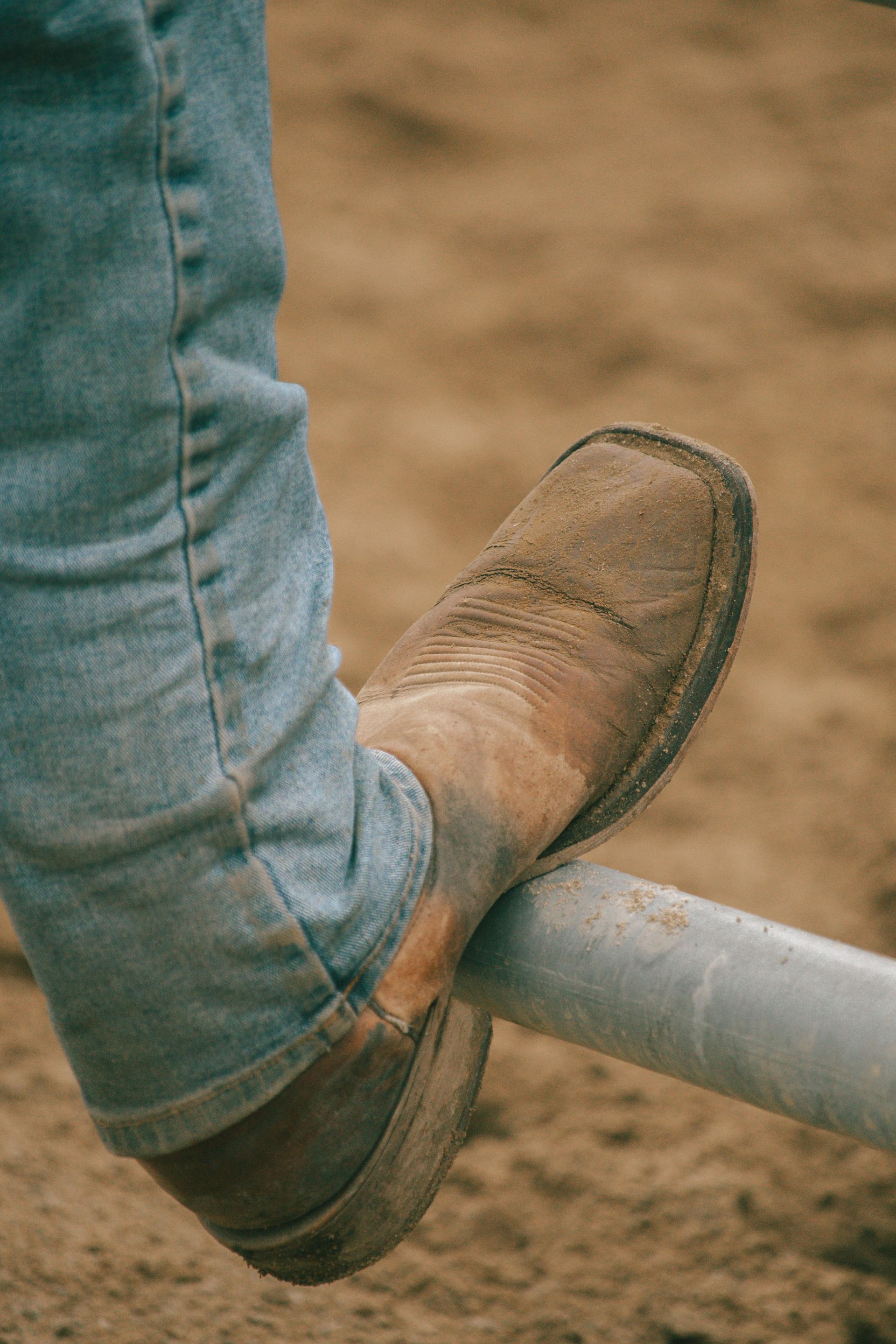 A person wearing cowboy boots is standing on a metal pole.