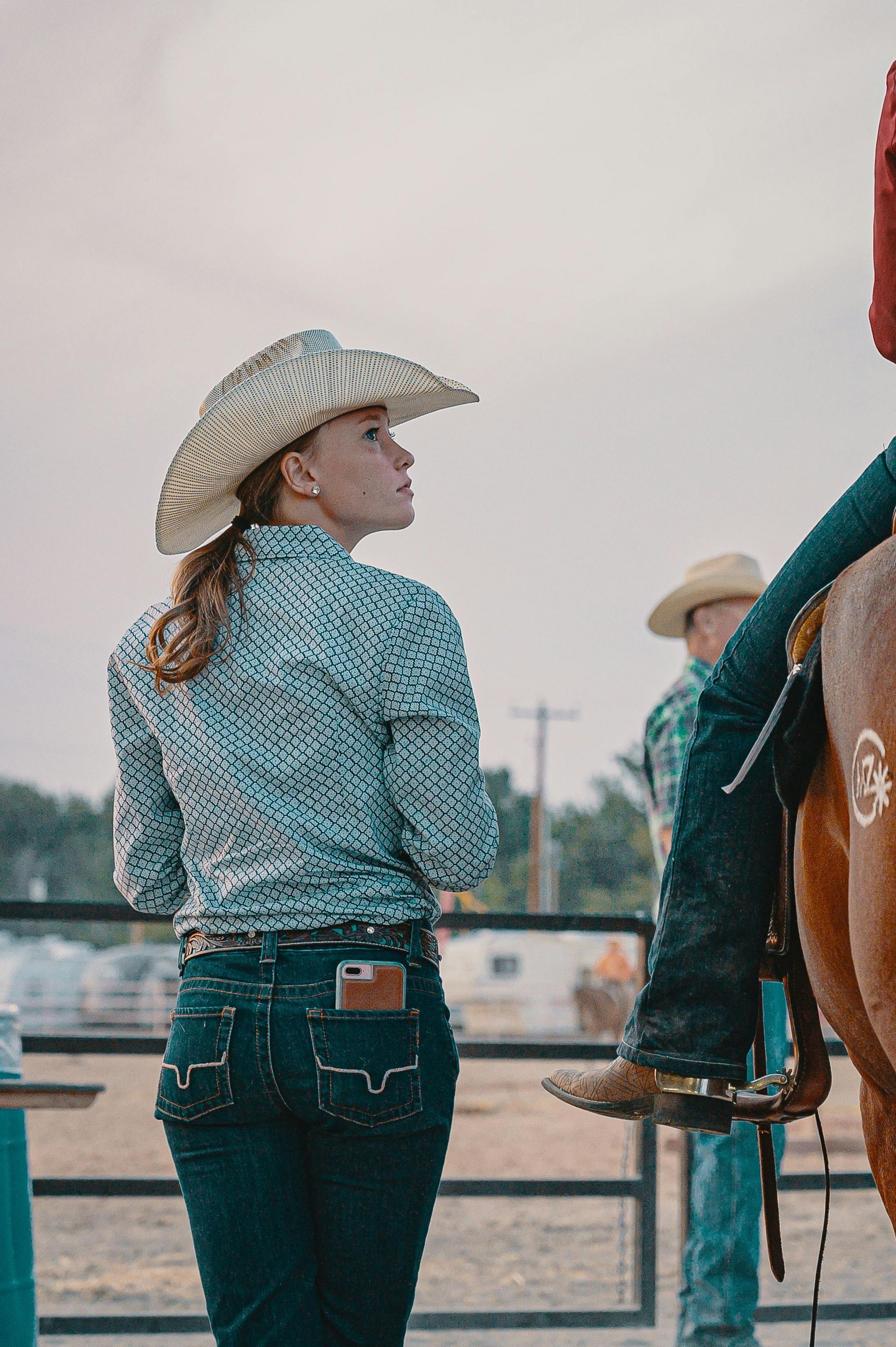 A woman in a cowboy hat is standing next to a man riding a horse.
