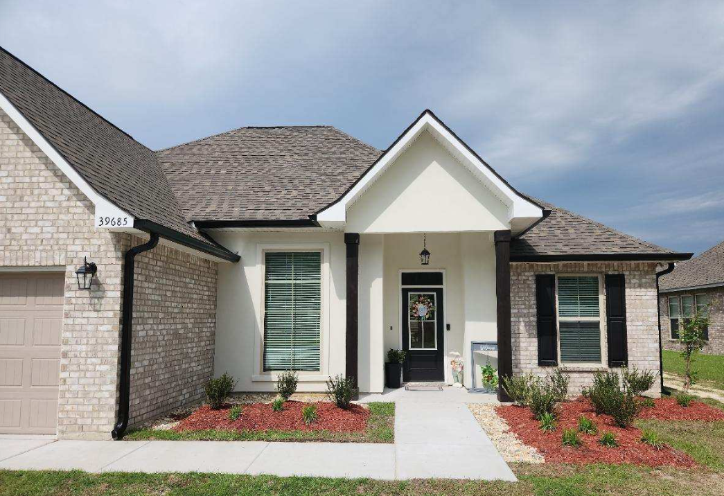 A picture of the front of a house with white stucco, bricks and black gutters in covington, LA