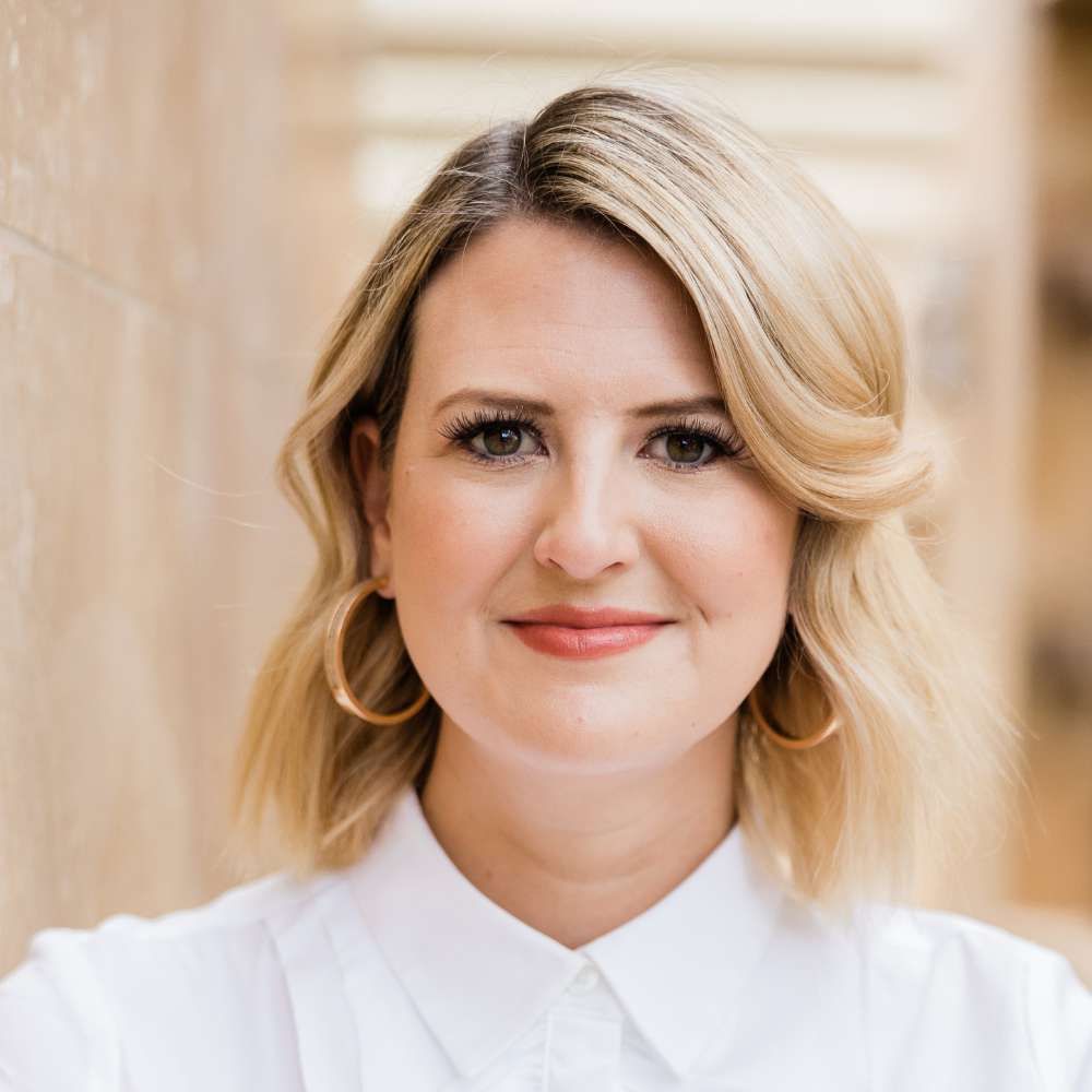 A woman wearing a white shirt and hoop earrings is smiling for the camera.