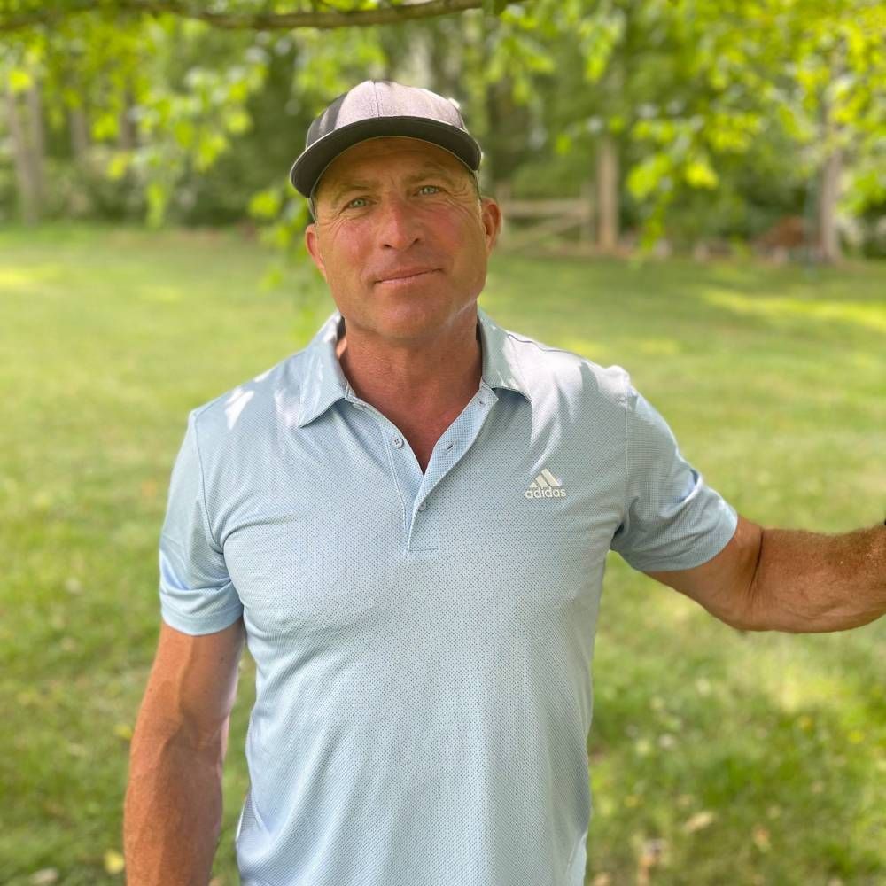 A man wearing a hat and a blue shirt is standing in a park.