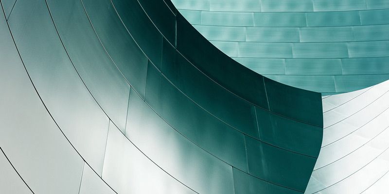 Nahaufnahme einer geschwungenen, metallischen Architekturstruktur mit genieteten Paneelen in verschiedenen Petroltönen.