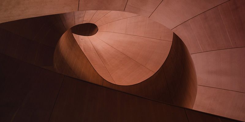 Abstrakte Ansicht einer Wendeltreppe aus einem kupferfarbenem Material mit einer kreisförmigen Öffnung in der Mitte.
