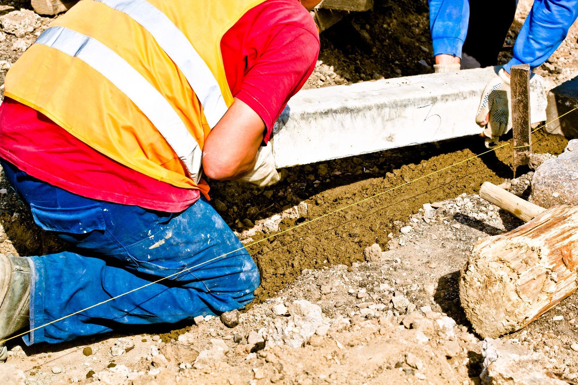 Construction workers in high-visibility jackets installing a concrete curb on a residential street