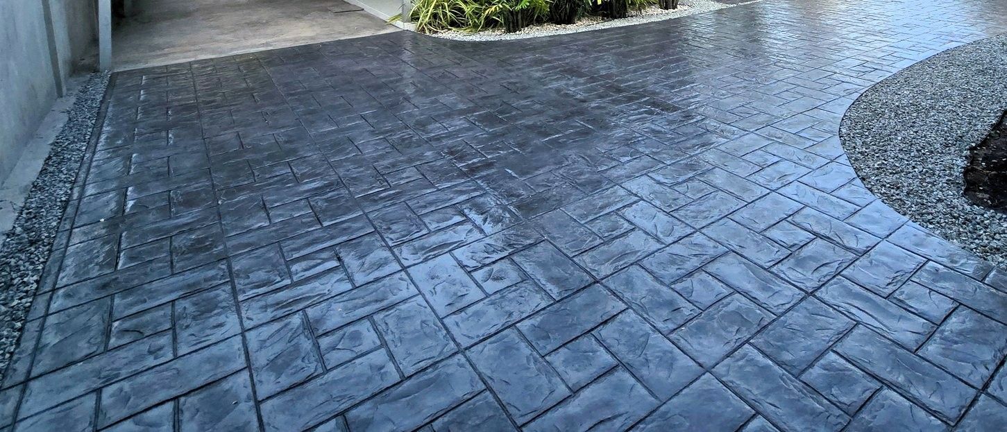 Dark stamped concrete driveway curves through landscaped gravel and plants