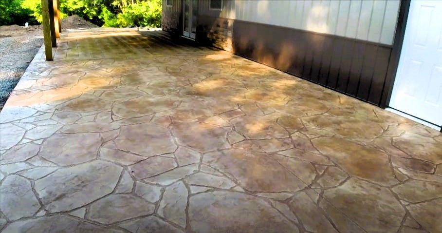 A stamped concrete patio with a house and trees in the background.
