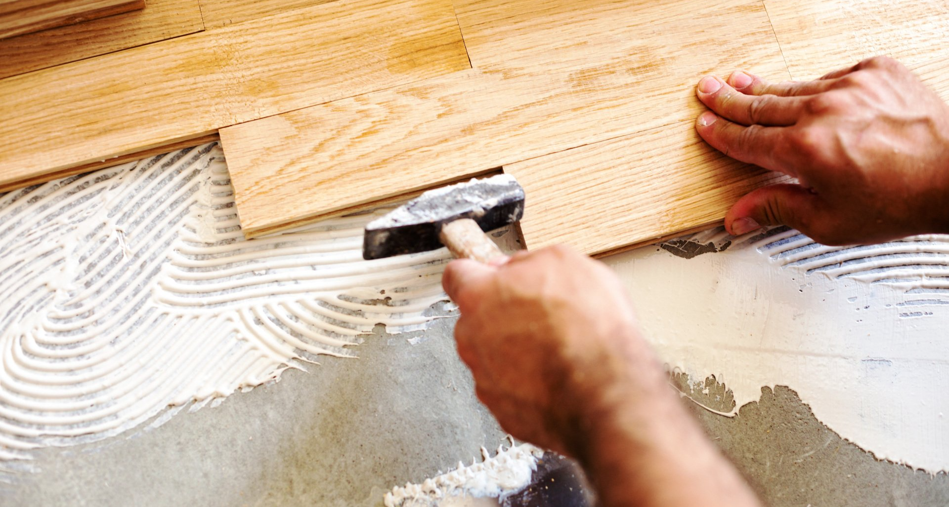 man laying wood flooring with hammer tool and glue