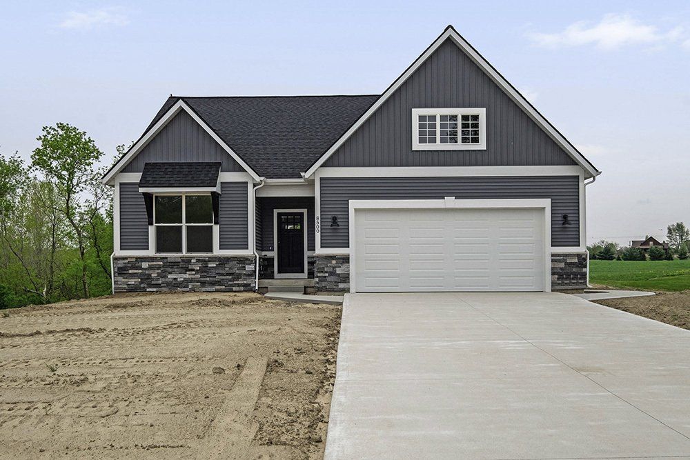 A gray house with a white garage door with a dirt yard.
