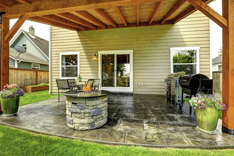 There is a fire pit on the custom concrete patio under a pergola.