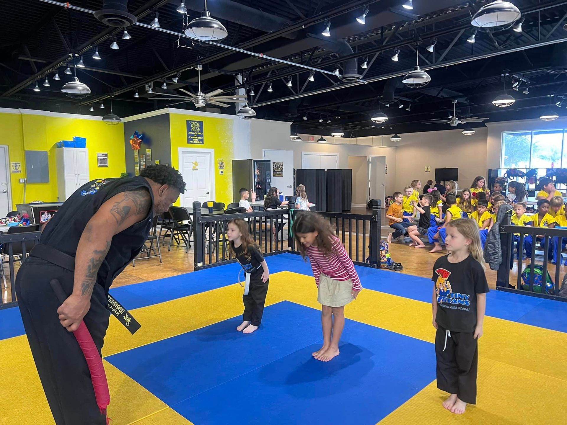 A man is teaching two young girls martial arts in a gym.