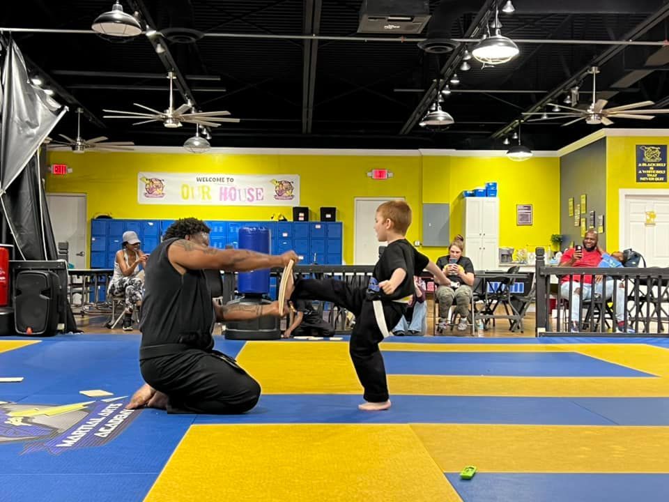 A man is kneeling down next to a young boy on a mat in a gym.
