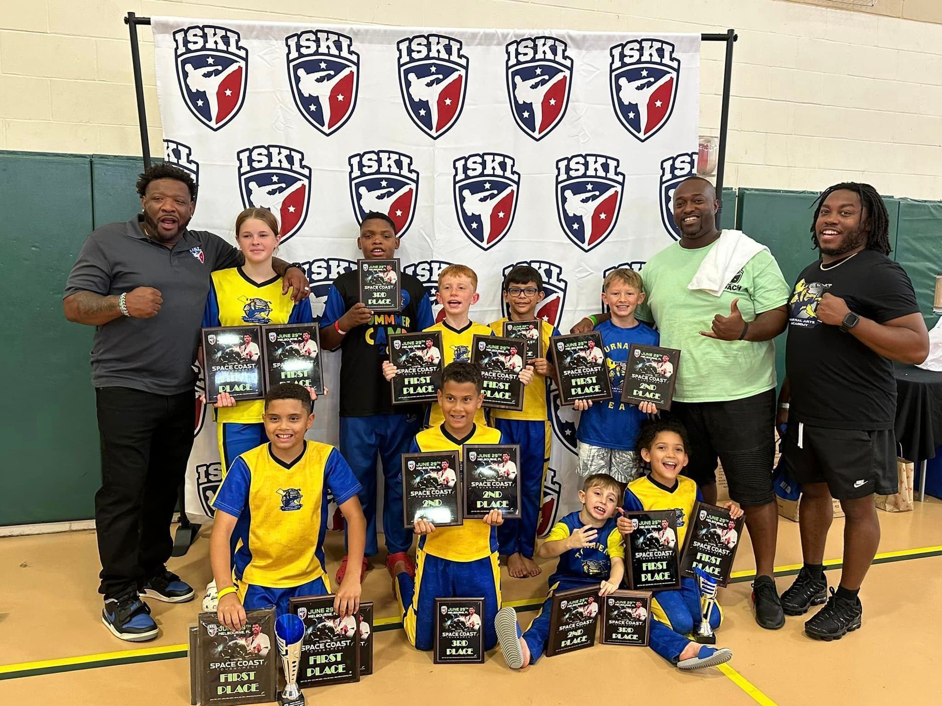 A group of young boys are posing for a picture while holding trophies.