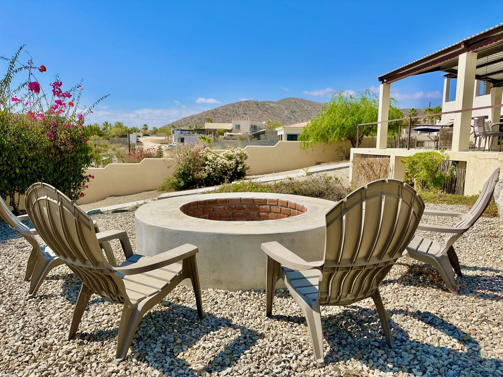 Desert patio with metal chairs around a stone fire pit, overlooking homes and hills under a clear sky