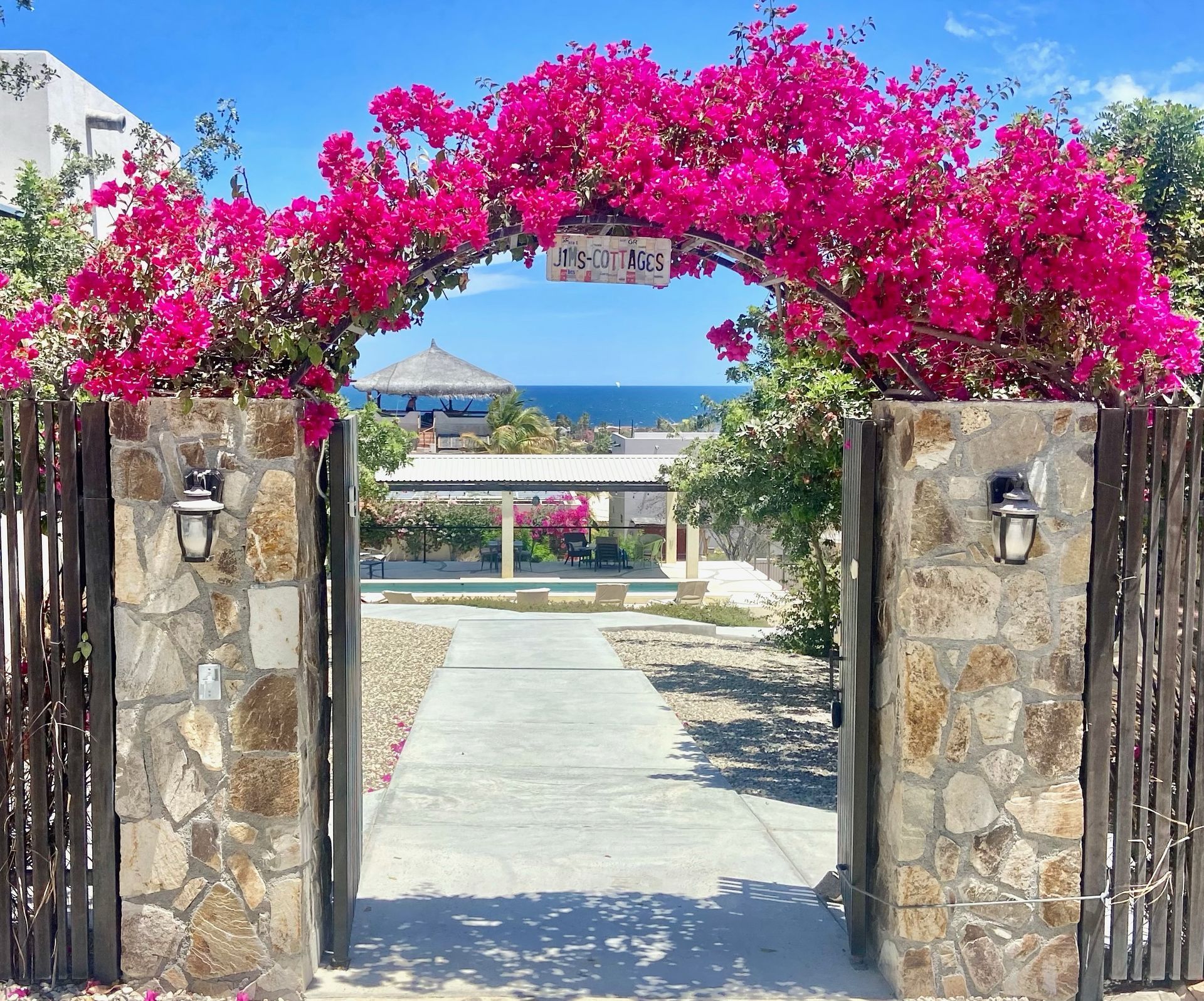 Stone gate with pink bougainvillea archway leading to a seaside view under a bright blue sky
