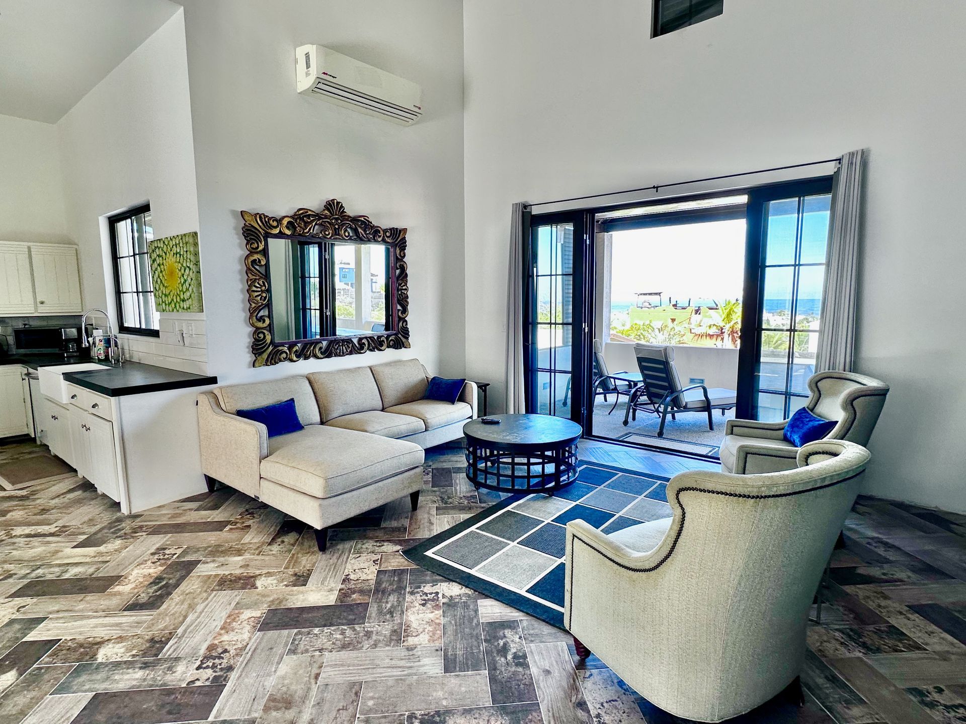 Bright living room with sectional sofa, chairs, coffee table, wall mirror, and open balcony doors