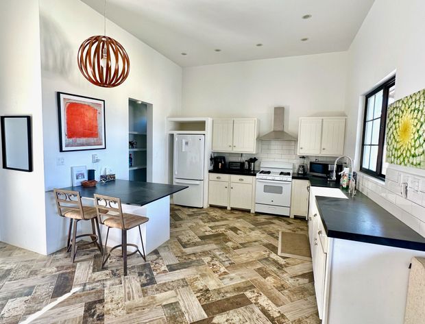 Bright modern kitchen with white cabinets, black counters, bar stools, and a sunflower wall hanging