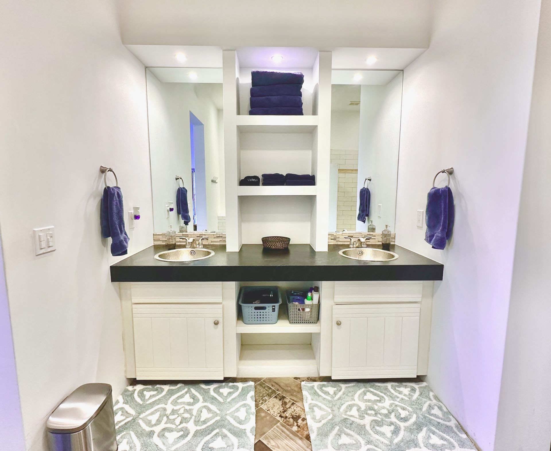 Modern bathroom vanity with double sinks, white cabinetry, dark countertops, and patterned floor tiles.