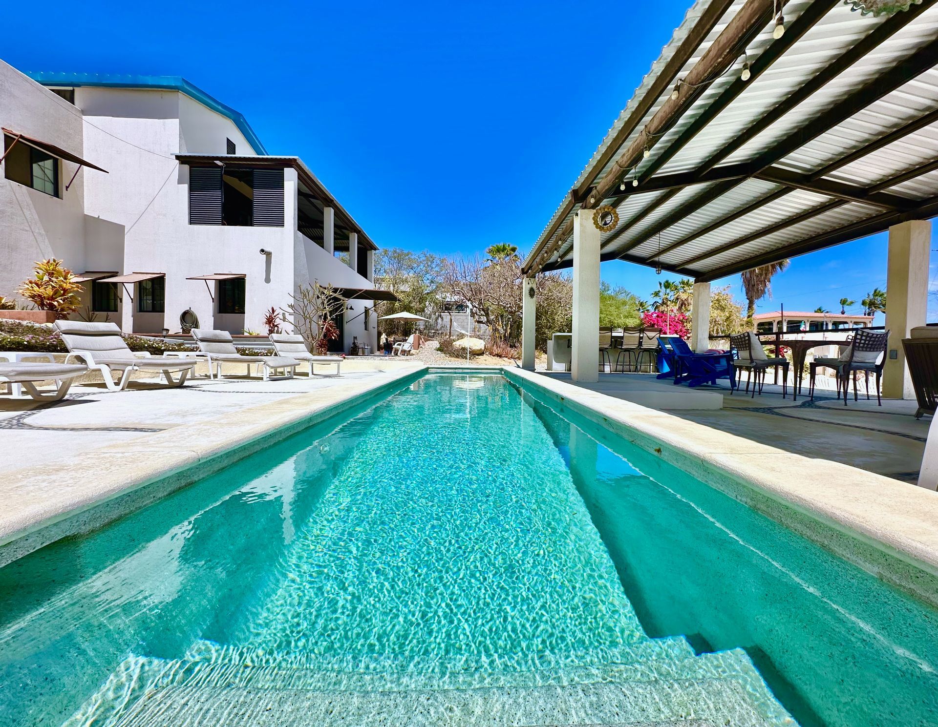 Modern villa with turquoise pool, lounge chairs, and covered patio under a bright blue sky