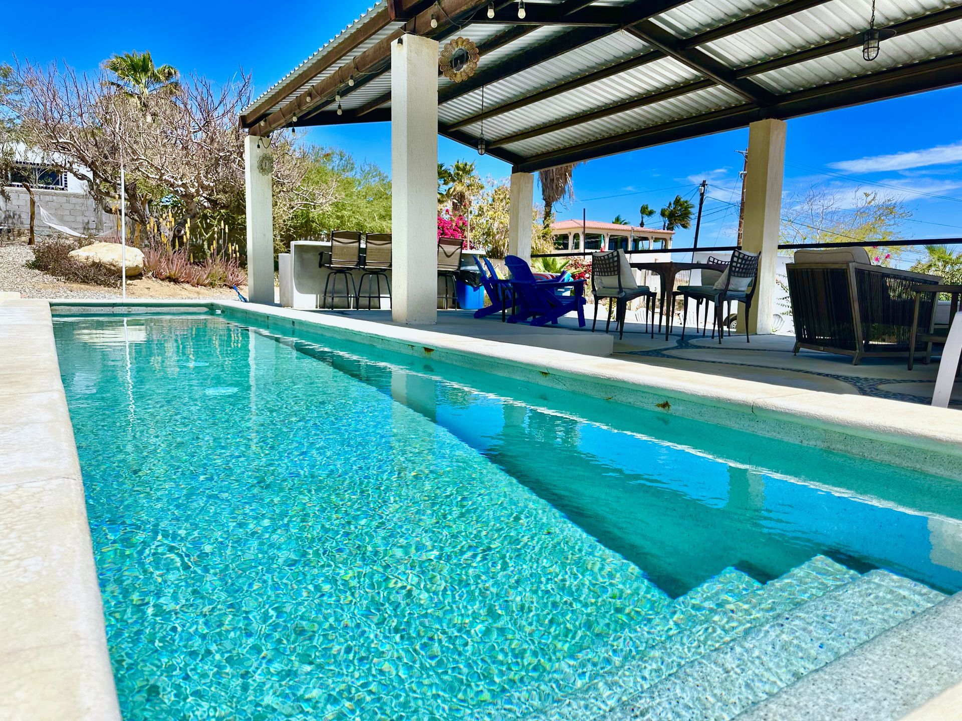 Modern backyard pool with a shaded patio, blue chairs, and a glassy turquoise water surface