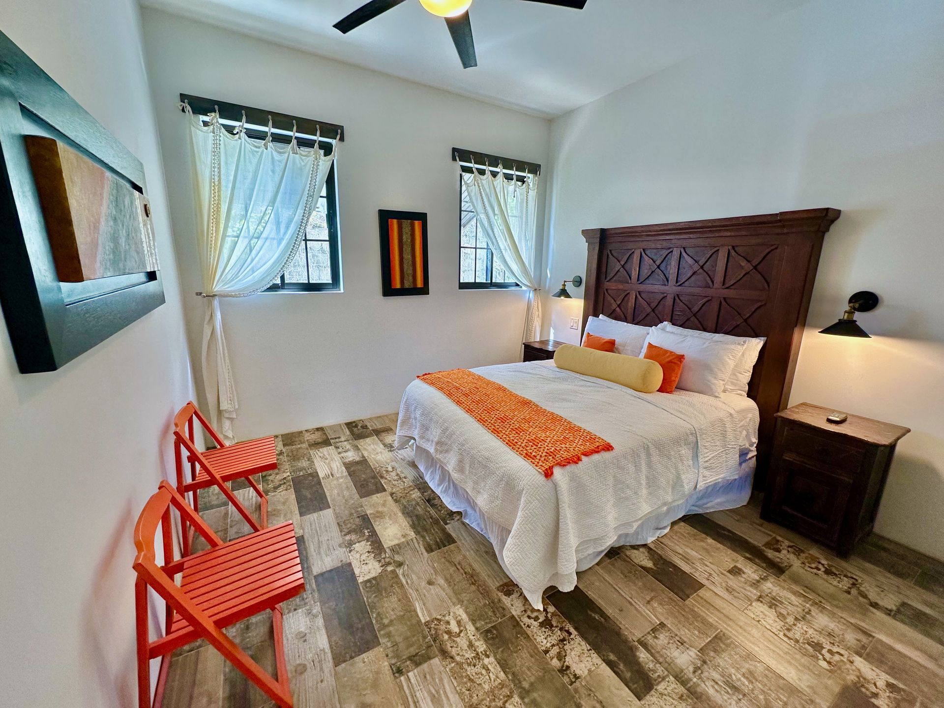 Bright bedroom with a large bed, orange chairs, and patterned rug on a light wood floor