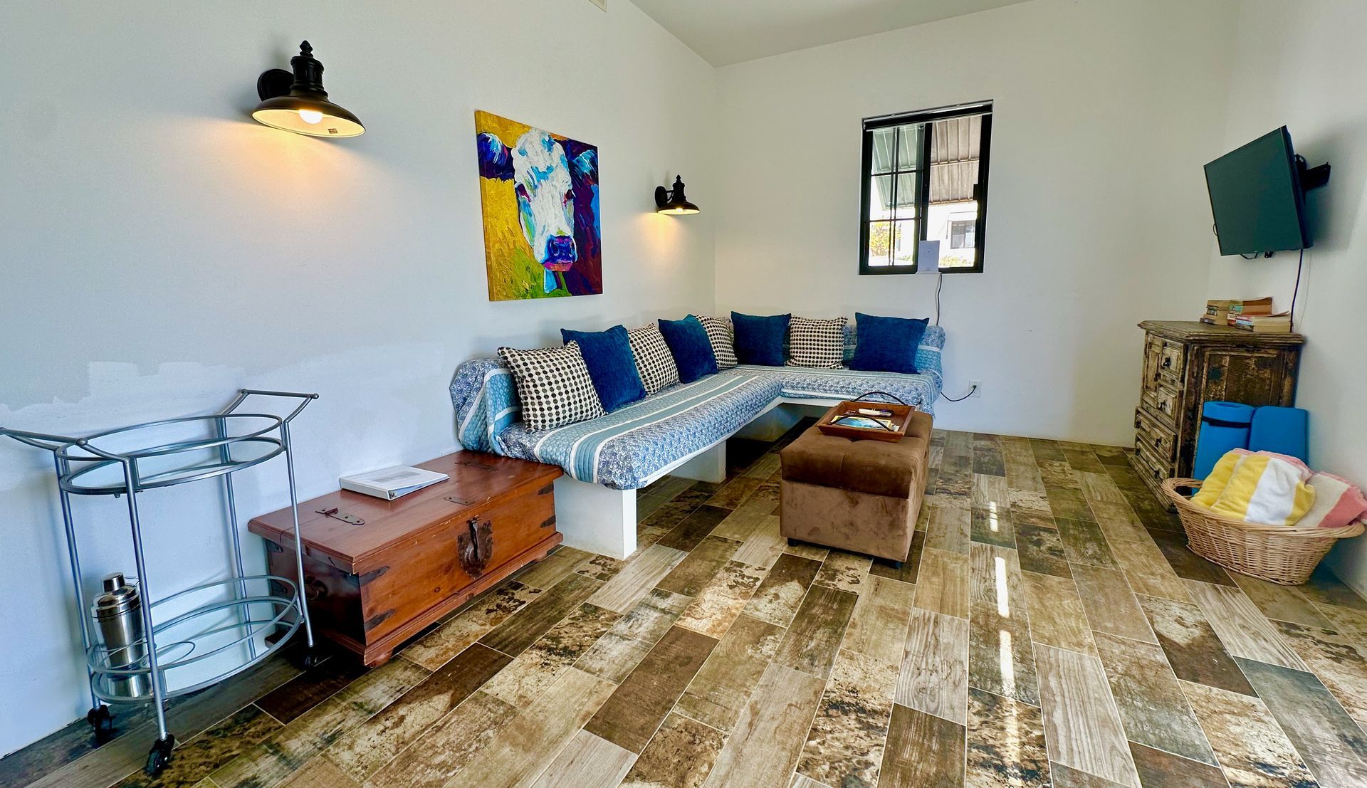 Cozy living room with patterned sofa, brown ottoman, wall art, TV, and wood-look floors