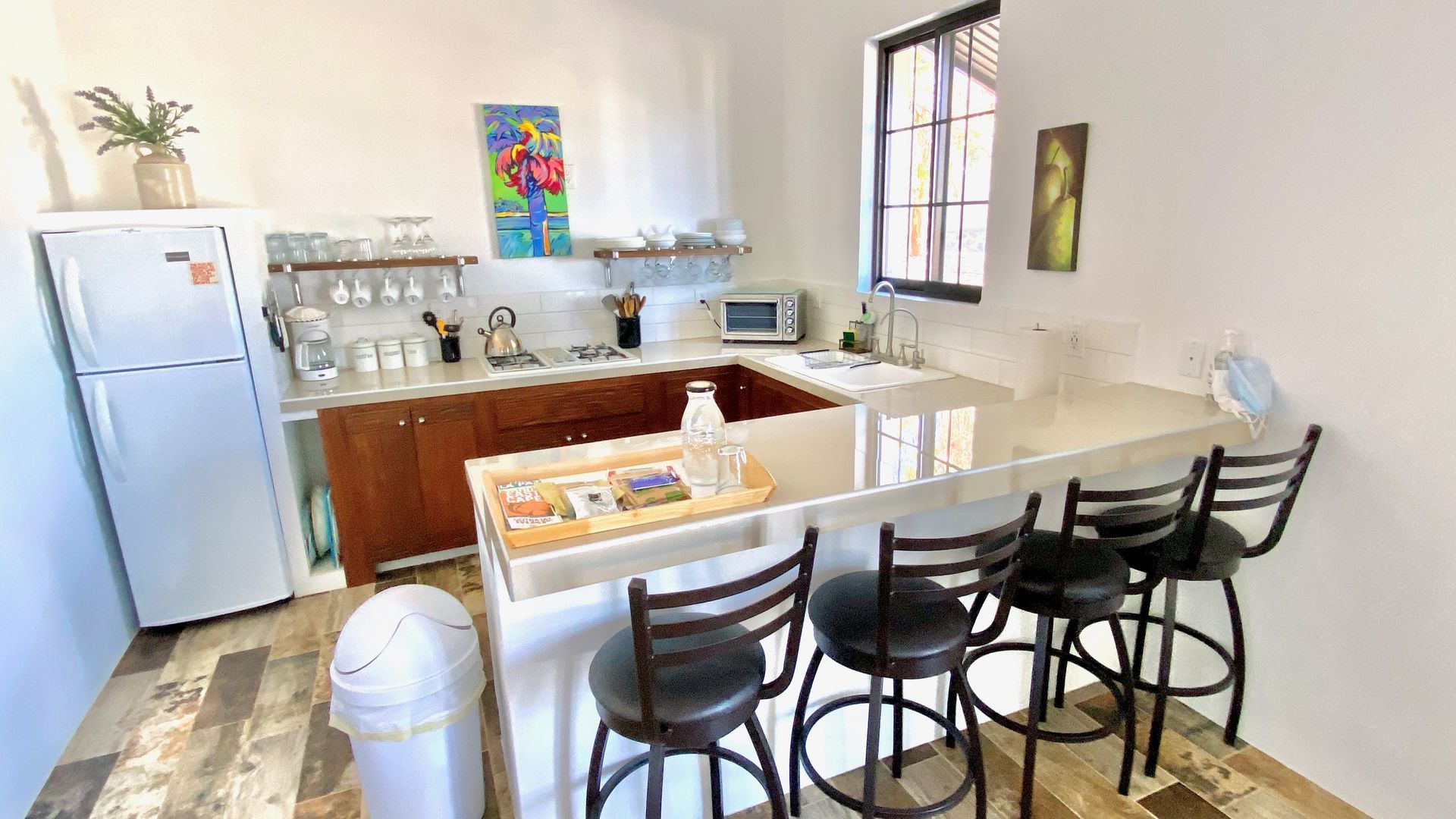 Modern kitchen with white cabinets, a wooden island, bar stools, and a stainless refrigerator by a window.