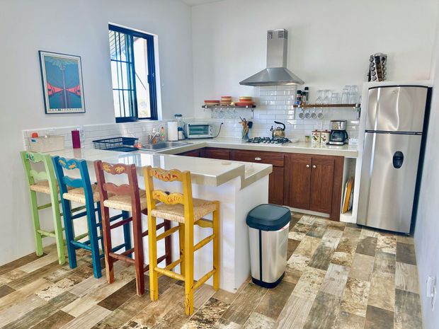 Bright kitchen with white island, colorful stools, stainless fridge, and patterned tile floor