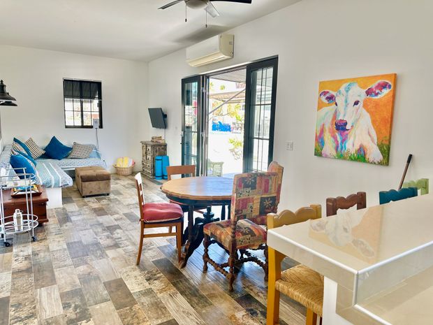 Bright living room with a round table, patterned chairs, sofa, large window, and colorful wall art.