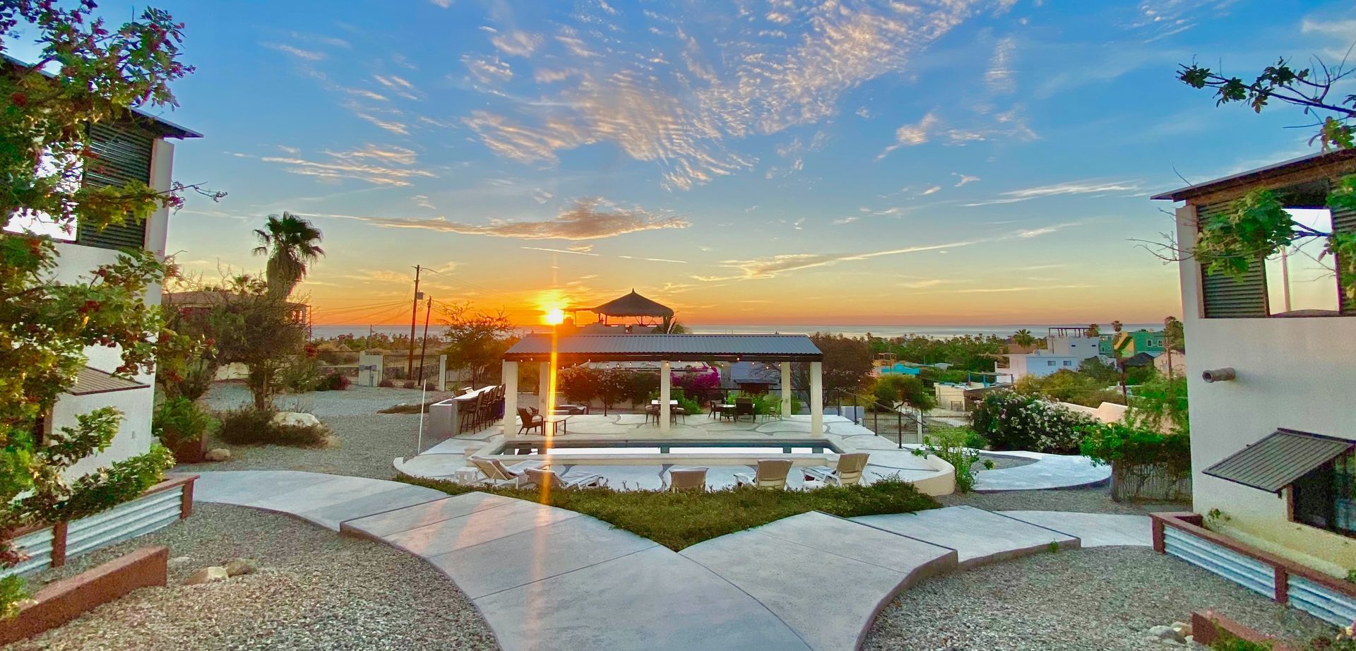 Sunset over a modern courtyard with white seating, a reflecting pool, and palm-lined views
