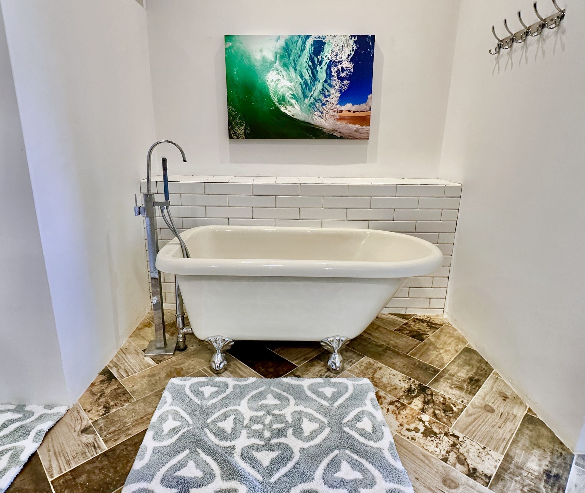 Small modern bathroom with a freestanding tub, patterned floor, ocean art, and gray rug.