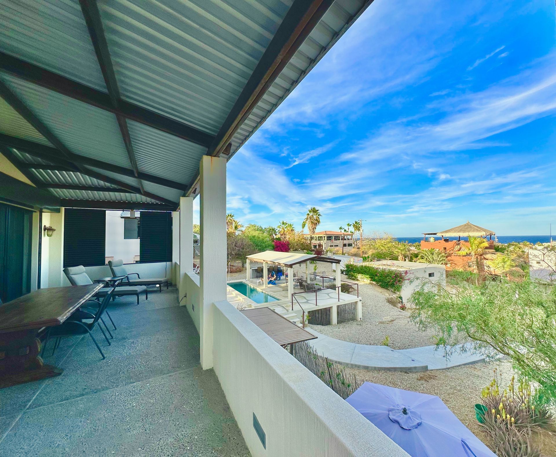 Covered patio overlooking a bright garden and ocean view, with wicker seating and lounge chairs