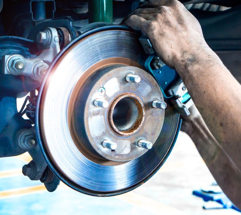 Technician performing brake rotor replacement on a vehicle in an auto repair shop.