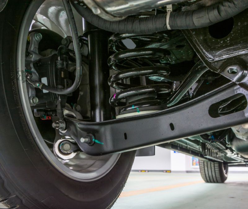 Suspension auto repair showing control arm, coil spring, and wheel assembly under a vehicle