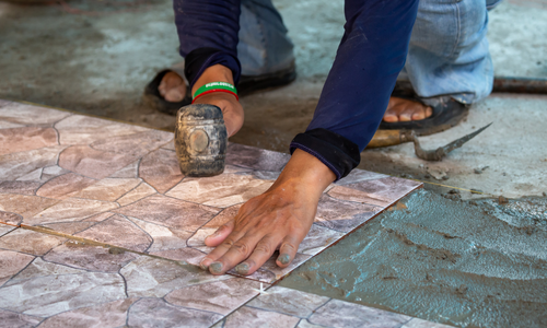 Worker has one hand pressing down the concrete stamp while the other holds a mallet used to transfer the stamp design to the concrete