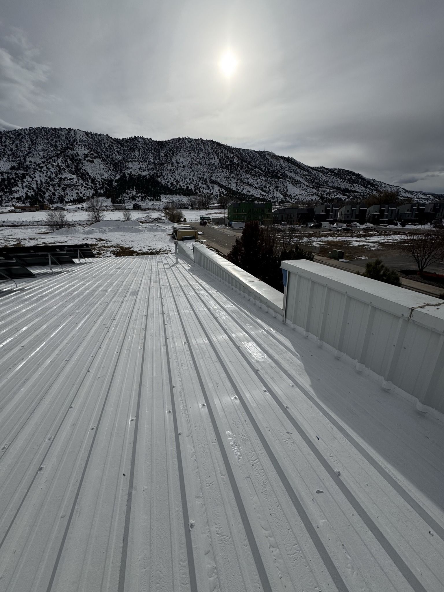 White metal rooftop under dark storm clouds, with distant buildings and hills on the horizon