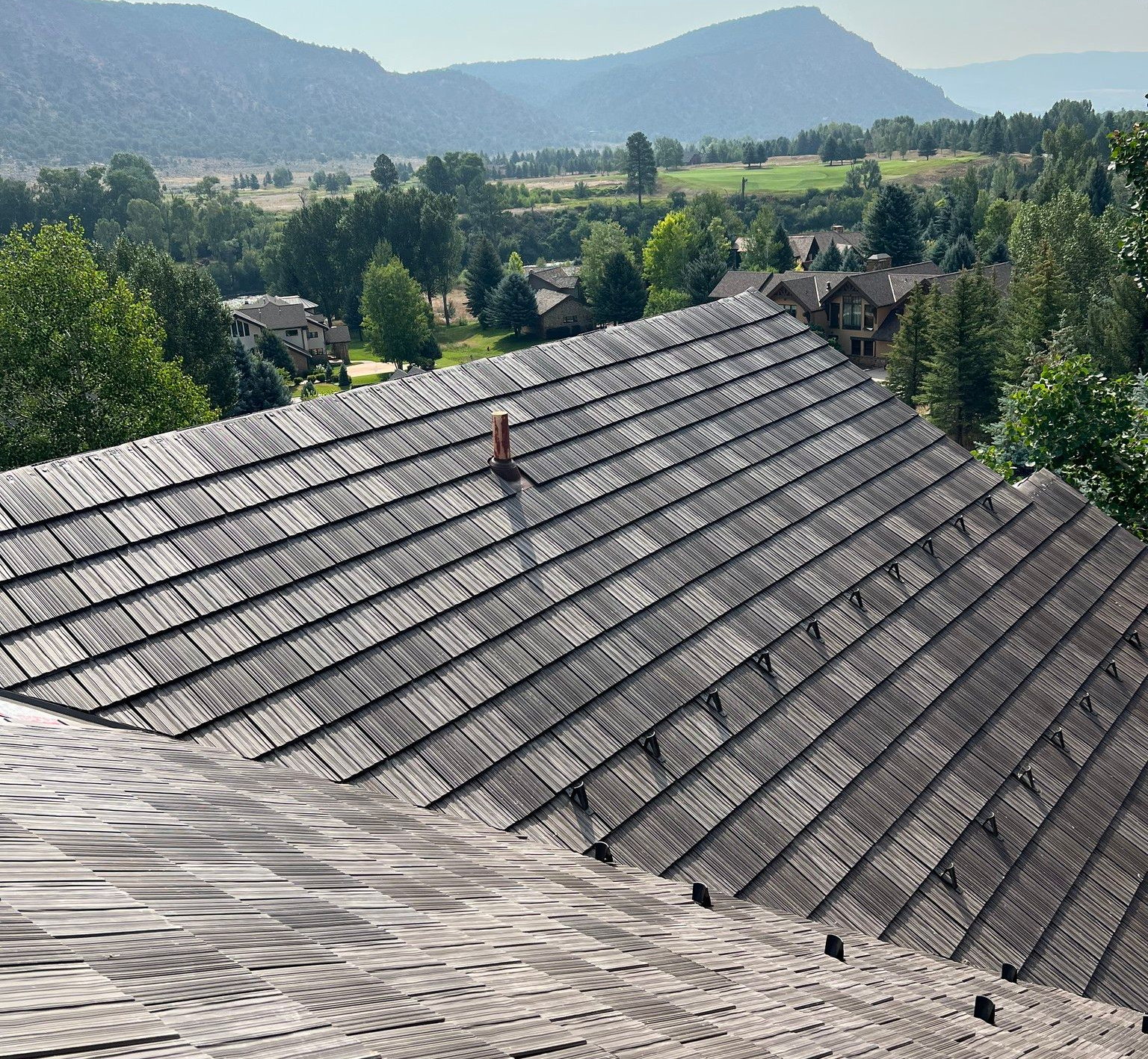 Rooftops in a mountain village with trees and hills in the background under clear daylight