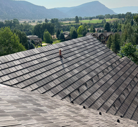 Rooftops in a mountain village with trees and hills in the background under clear daylight