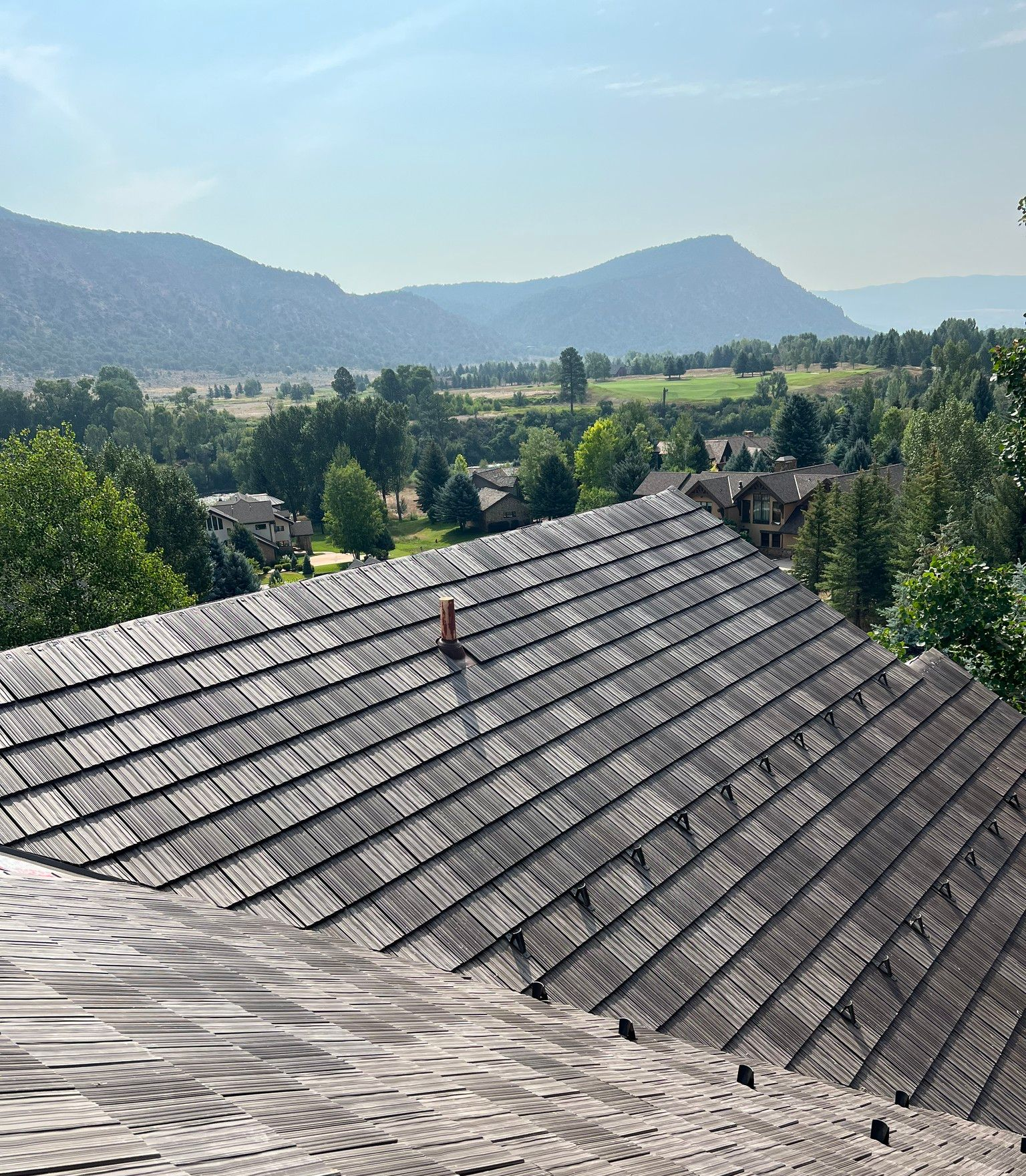 Rooftop overlooking a green valley and distant mountains under a clear blue sky.