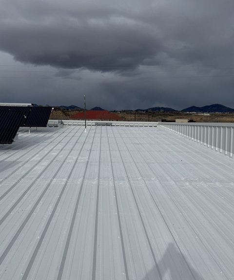 White metal rooftop under dark storm clouds, with distant buildings and hills on the horizon