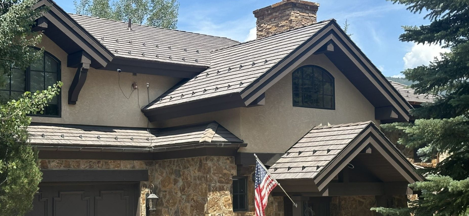 Stone house exterior with brown shingle roof, arched windows, chimney, and an American flag by the entrance