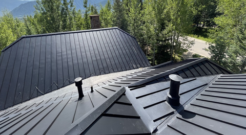 Black metal roofs overlooking a forested mountain landscape on a sunny day