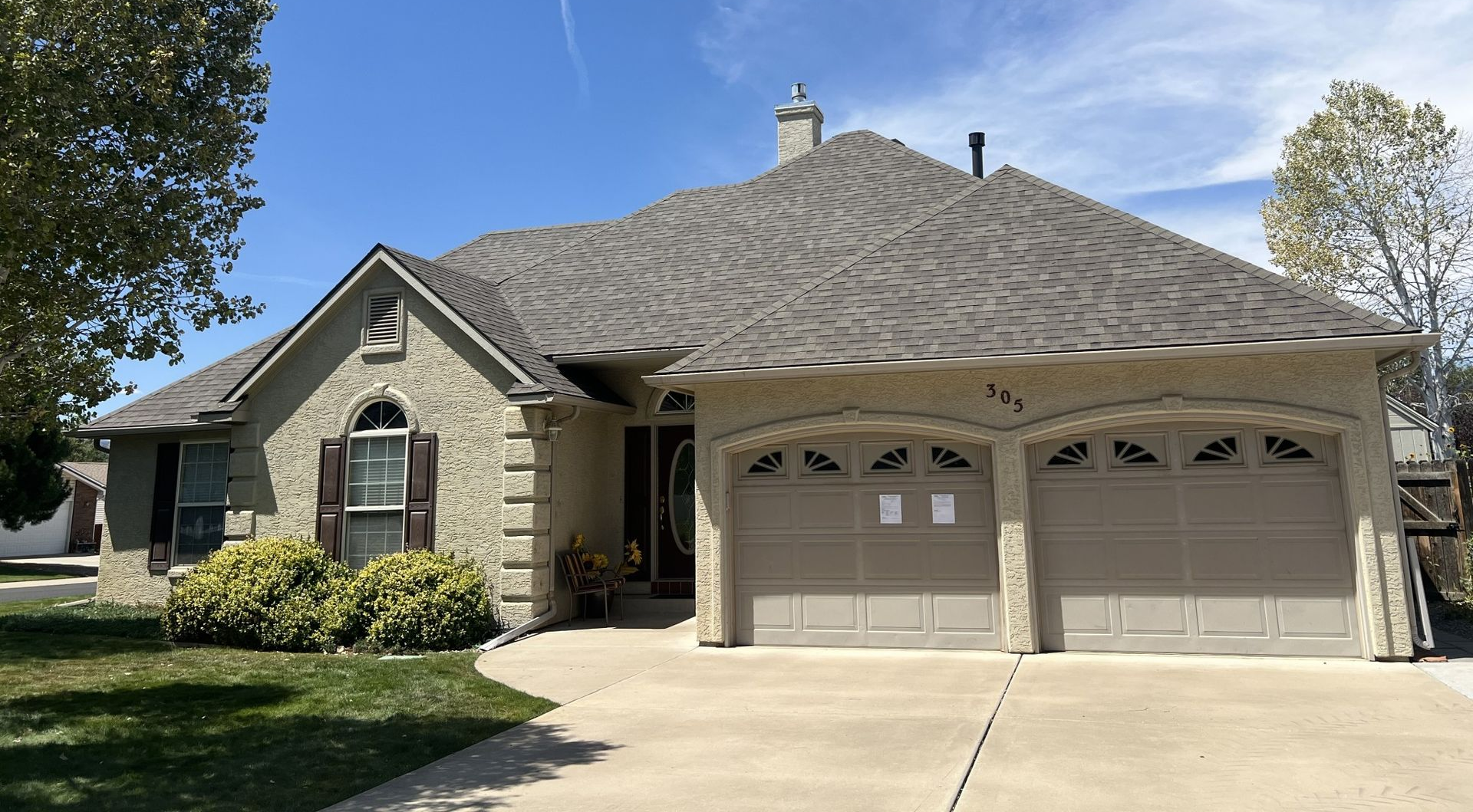 Single-story suburban house with stone facade, two-car garage, and a driveway under a sunny sky