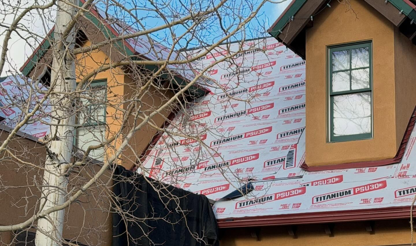 Partially built house with exposed wall wrap, window, and bare tree branches in front